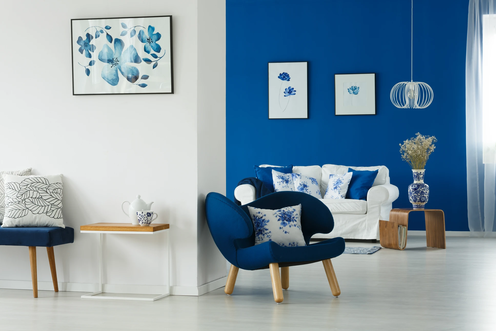 Salon moderne avec mur d'accent bleu royal, fauteuil bleu marine avec coussins floraux bleus et blancs, canapé blanc, mobilier en bois clair