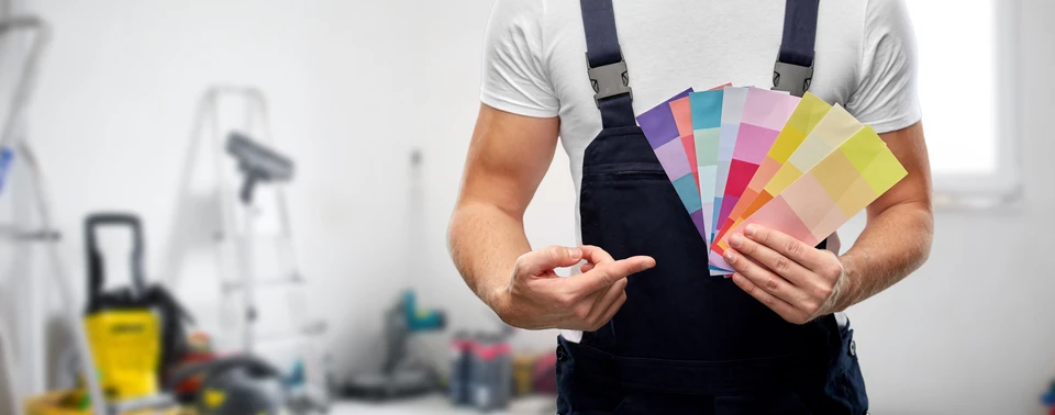 Homme en tablier noir tenant un éventail de nuanciers colorés dans un atelier de peinture