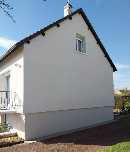 Façade extérieure de maison individuelle rénovée avec enduit blanc, toiture en tuiles mécaniques brunes, balcon métallique et fenêtres PVC blanches