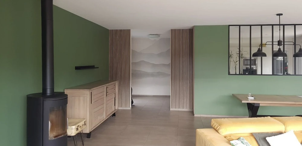 Salon moderne avec canapé en cuir noir, fauteuil jaune moutarde, escalier en bois naturel, cheminée à foyer ouvert avec parement en briques et habillage bois à lames verticales